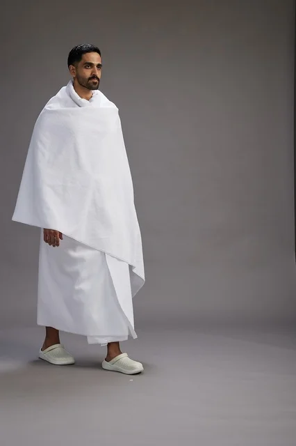 بورتريه لرجل عربي سعودي خليجي يرتدي ملابس الإحرام لأداء مناسك الحج, العباده والتقرب الى الله , الحج والعمره في مكه, الجسم بالطول الكامل , خلفيه رماديه