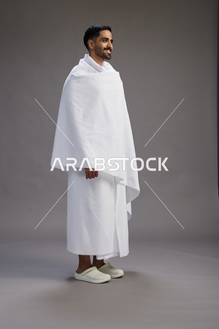 بورتريه لرجل عربي سعودي خليجي يرتدي ملابس الإحرام لأداء مناسك الحج, العباده والتقرب الى الله , الحج والعمره في مكه, الجسم بالطول الكامل , خلفيه رماديه