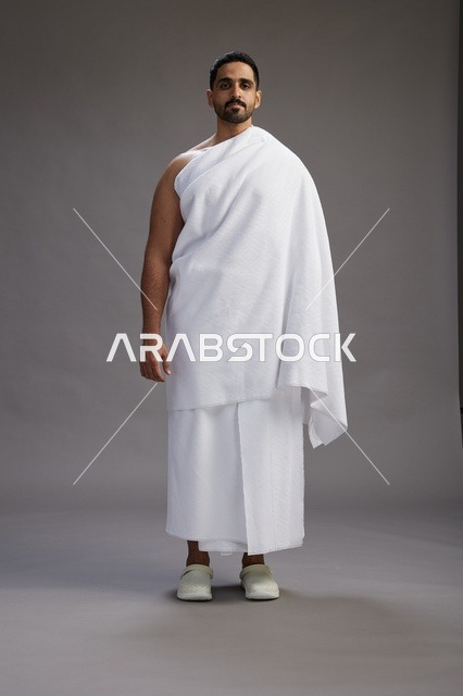 بورتريه لرجل عربي سعودي خليجي يرتدي ملابس الإحرام لأداء مناسك الحج, العباده والتقرب الى الله , الحج والعمره في مكه, الجسم بالطول الكامل , خلفيه رماديه