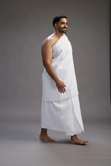 A portrait of an Arab Saudi Gulf man wearing Ihram clothing to perform the rituals of Hajj, worship, and drawing closer to God, Hajj and Umrah in Mecca, full-body, gray background.