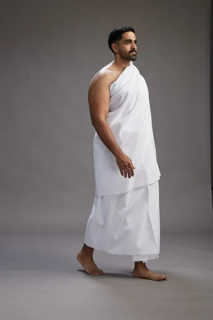بورتريه لرجل عربي سعودي خليجي يرتدي ملابس الإحرام لأداء مناسك الحج, العباده والتقرب الى الله , الحج والعمره في مكه, الجسم بالطول الكامل , خلفيه رماديه