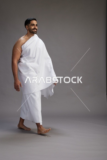 بورتريه لرجل عربي سعودي خليجي يرتدي ملابس الإحرام لأداء مناسك الحج, العباده والتقرب الى الله , الحج والعمره في مكه, الجسم بالطول الكامل , خلفيه رماديه
