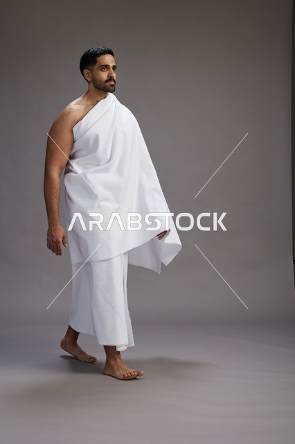 بورتريه لرجل عربي سعودي خليجي يرتدي ملابس الإحرام لأداء مناسك الحج, العباده والتقرب الى الله , الحج والعمره في مكه, الجسم بالطول الكامل , خلفيه رماديه