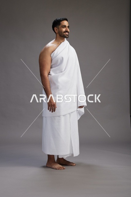 بورتريه لرجل عربي سعودي خليجي يرتدي ملابس الإحرام لأداء مناسك الحج, العباده والتقرب الى الله , الحج والعمره في مكه, الجسم بالطول الكامل , خلفيه رماديه