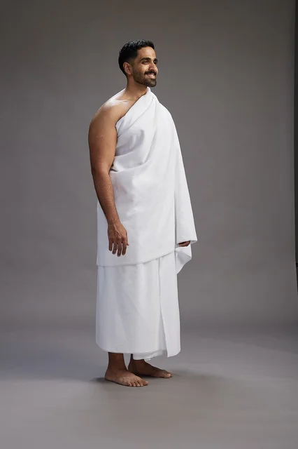 A portrait of an Arab Saudi Gulf man wearing Ihram clothing to perform the rituals of Hajj, worship, and drawing closer to God, Hajj and Umrah in Mecca, full-body, gray background.