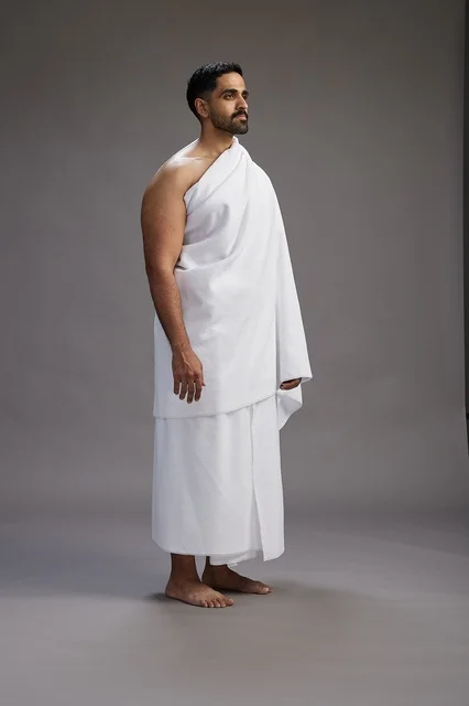 A portrait of an Arab Saudi Gulf man wearing Ihram clothing to perform the rituals of Hajj, worship, and drawing closer to God, Hajj and Umrah in Mecca, full-body, gray background.