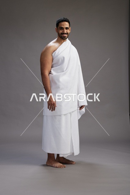 بورتريه لرجل عربي سعودي خليجي يرتدي ملابس الإحرام لأداء مناسك الحج, العباده والتقرب الى الله , الحج والعمره في مكه, الجسم بالطول الكامل , خلفيه رماديه
