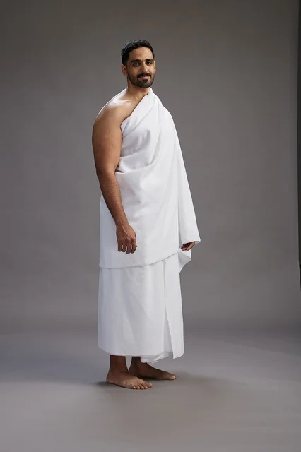 A portrait of an Arab Saudi Gulf man wearing Ihram clothing to perform the rituals of Hajj, worship, and drawing closer to God, Hajj and Umrah in Mecca, full-body, gray background.