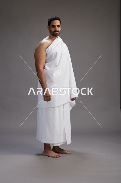بورتريه لرجل عربي سعودي خليجي يرتدي ملابس الإحرام لأداء مناسك الحج, العباده والتقرب الى الله , الحج والعمره في مكه, الجسم بالطول الكامل , خلفيه رماديه