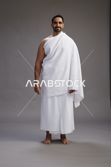 بورتريه لرجل عربي سعودي خليجي يرتدي ملابس الإحرام لأداء مناسك الحج, العباده والتقرب الى الله , الحج والعمره في مكه, الجسم بالطول الكامل , خلفيه رماديه
