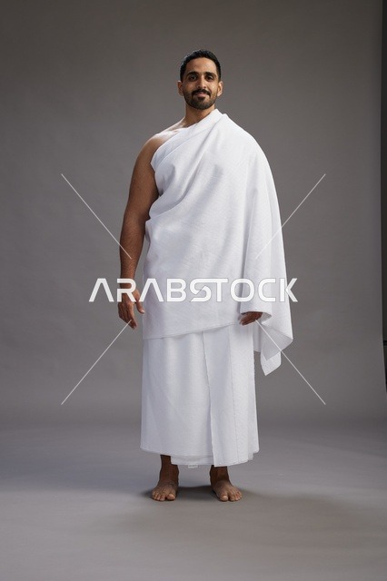 بورتريه لرجل عربي سعودي خليجي يرتدي ملابس الإحرام لأداء مناسك الحج, العباده والتقرب الى الله , الحج والعمره في مكه, الجسم بالطول الكامل , خلفيه رماديه
