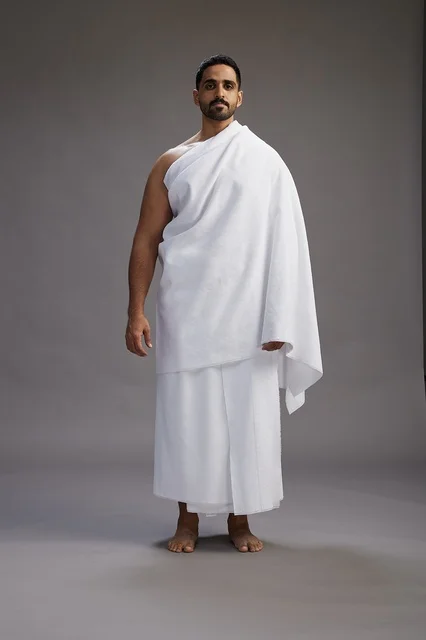 A portrait of an Arab Saudi Gulf man wearing Ihram clothing to perform the rituals of Hajj, worship, and drawing closer to God, Hajj and Umrah in Mecca, full-body, gray background.