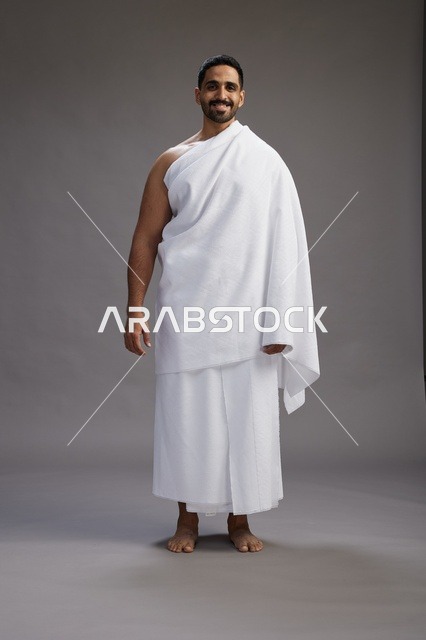بورتريه لرجل عربي سعودي خليجي يرتدي ملابس الإحرام لأداء مناسك الحج, العباده والتقرب الى الله , الحج والعمره في مكه, الجسم بالطول الكامل , خلفيه رماديه