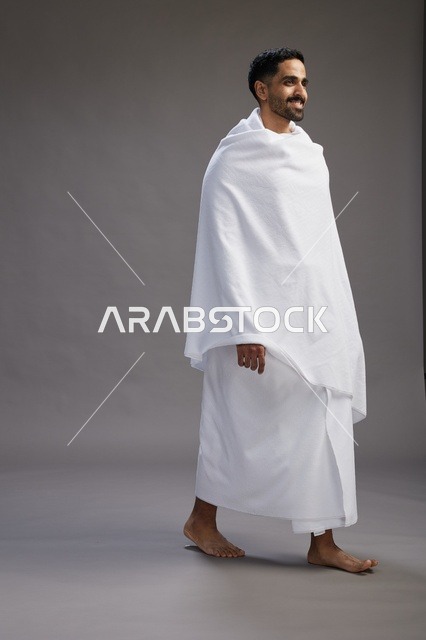 بورتريه لرجل عربي سعودي خليجي يرتدي ملابس الإحرام لأداء مناسك الحج, العباده والتقرب الى الله , الحج والعمره في مكه, الجسم بالطول الكامل , خلفيه رماديه