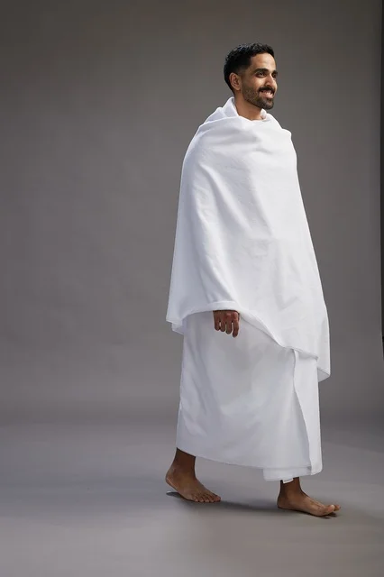 A portrait of an Arab Saudi Gulf man wearing Ihram clothing to perform the rituals of Hajj, worship, and drawing closer to God, Hajj and Umrah in Mecca, full-body, gray background.