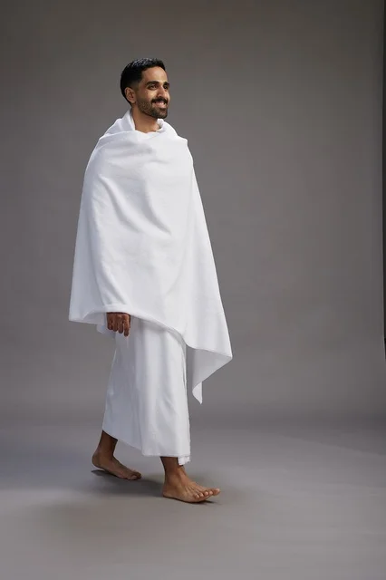 A portrait of an Arab Saudi Gulf man wearing Ihram clothing to perform the rituals of Hajj, worship, and drawing closer to God, Hajj and Umrah in Mecca, full-body, gray background.