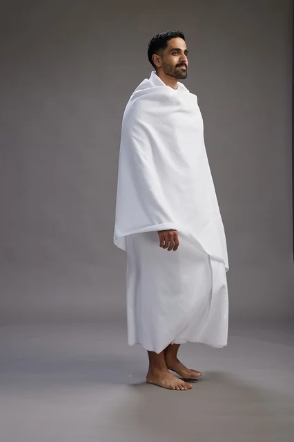 بورتريه لرجل عربي سعودي خليجي يرتدي ملابس الإحرام لأداء مناسك الحج, العباده والتقرب الى الله , الحج والعمره في مكه, الجسم بالطول الكامل , خلفيه رماديه