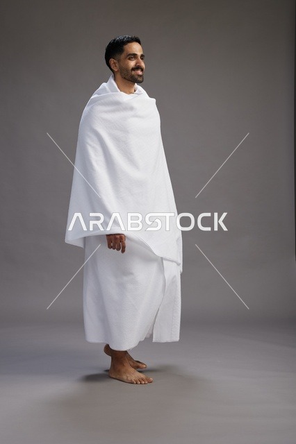بورتريه لرجل عربي سعودي خليجي يرتدي ملابس الإحرام لأداء مناسك الحج, العباده والتقرب الى الله , الحج والعمره في مكه, الجسم بالطول الكامل , خلفيه رماديه