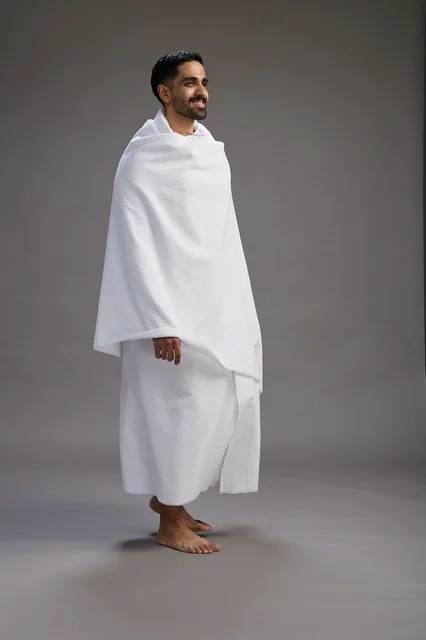 A portrait of an Arab Saudi Gulf man wearing Ihram clothing to perform the rituals of Hajj, worship, and drawing closer to God, Hajj and Umrah in Mecca, full-body, gray background.