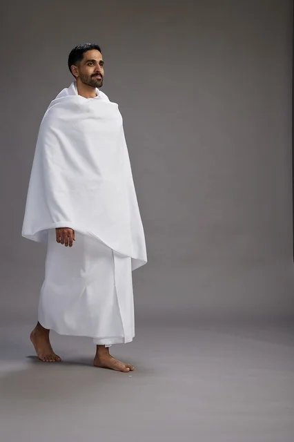 بورتريه لرجل عربي سعودي خليجي يرتدي ملابس الإحرام لأداء مناسك الحج, العباده والتقرب الى الله , الحج والعمره في مكه, الجسم بالطول الكامل , خلفيه رماديه
