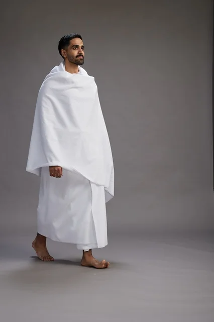 بورتريه لرجل عربي سعودي خليجي يرتدي ملابس الإحرام لأداء مناسك الحج, العباده والتقرب الى الله , الحج والعمره في مكه, الجسم بالطول الكامل , خلفيه رماديه