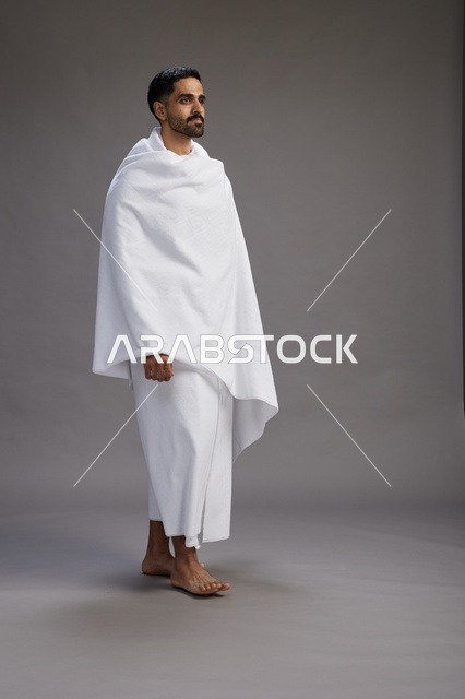 بورتريه لرجل عربي سعودي خليجي يرتدي ملابس الإحرام لأداء مناسك الحج, العباده والتقرب الى الله , الحج والعمره في مكه, الجسم بالطول الكامل , خلفيه رماديه