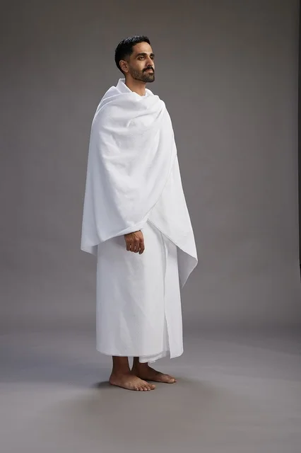بورتريه لرجل عربي سعودي خليجي يرتدي ملابس الإحرام لأداء مناسك الحج, العباده والتقرب الى الله , الحج والعمره في مكه, الجسم بالطول الكامل , خلفيه رماديه