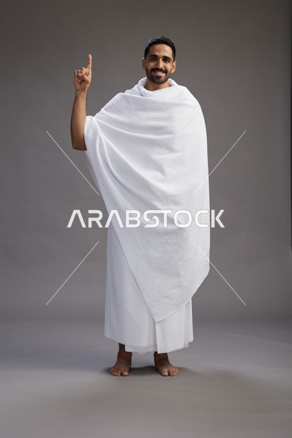 بورتريه لرجل عربي سعودي خليجي يرتدي ملابس الإحرام لأداء مناسك الحج, العباده والتقرب الى الله , الحج والعمره في مكه, الجسم بالطول الكامل , خلفيه رماديه