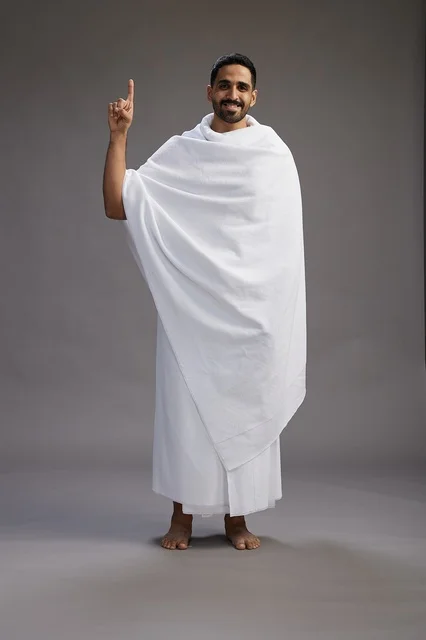 بورتريه لرجل عربي سعودي خليجي يرتدي ملابس الإحرام لأداء مناسك الحج, العباده والتقرب الى الله , الحج والعمره في مكه, الجسم بالطول الكامل , خلفيه رماديه