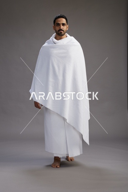 بورتريه لرجل عربي سعودي خليجي يرتدي ملابس الإحرام لأداء مناسك الحج, العباده والتقرب الى الله , الحج والعمره في مكه, الجسم بالطول الكامل , خلفيه رماديه