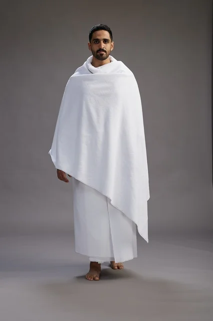 بورتريه لرجل عربي سعودي خليجي يرتدي ملابس الإحرام لأداء مناسك الحج, العباده والتقرب الى الله , الحج والعمره في مكه, الجسم بالطول الكامل , خلفيه رماديه