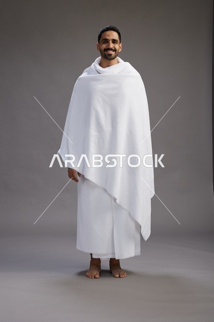 بورتريه لرجل عربي سعودي خليجي يرتدي ملابس الإحرام لأداء مناسك الحج, العباده والتقرب الى الله , الحج والعمره في مكه, الجسم بالطول الكامل , خلفيه رماديه