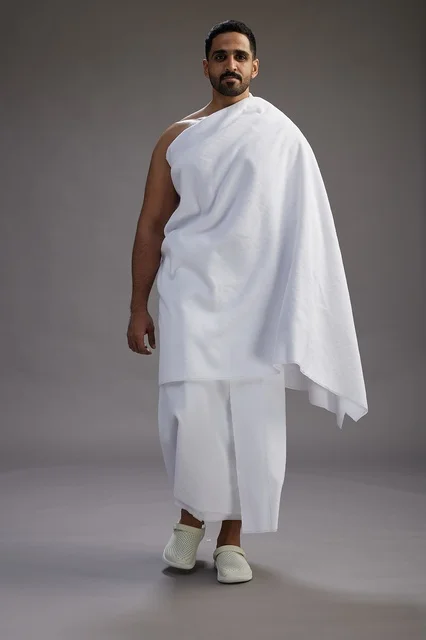 A portrait of an Arab Saudi Gulf man wearing Ihram clothing to perform the rituals of Hajj, worship, and drawing closer to God, Hajj and Umrah in Mecca, full-body, gray background.