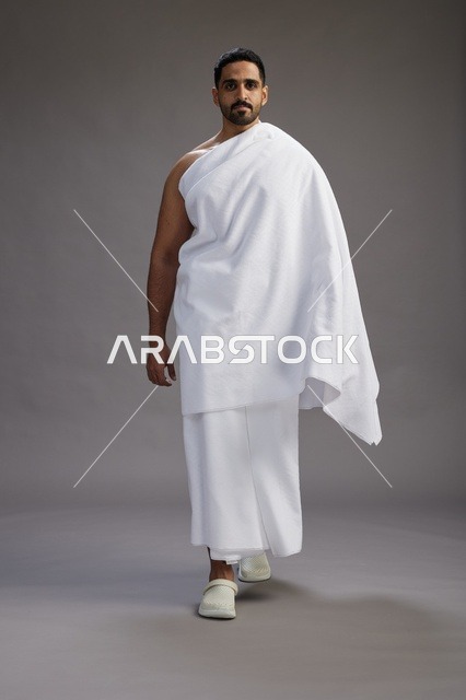 بورتريه لرجل عربي سعودي خليجي يرتدي ملابس الإحرام لأداء مناسك الحج, العباده والتقرب الى الله , الحج والعمره في مكه, الجسم بالطول الكامل , خلفيه رماديه
