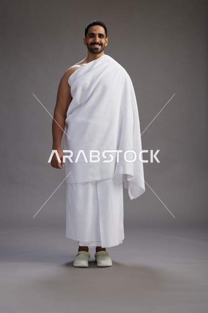 بورتريه لرجل عربي سعودي خليجي يرتدي ملابس الإحرام لأداء مناسك الحج, العباده والتقرب الى الله , الحج والعمره في مكه, الجسم بالطول الكامل , خلفيه رماديه