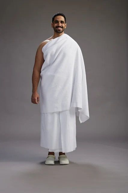 A portrait of an Arab Saudi Gulf man wearing Ihram clothing to perform the rituals of Hajj, worship, and drawing closer to God, Hajj and Umrah in Mecca, full-body, gray background.