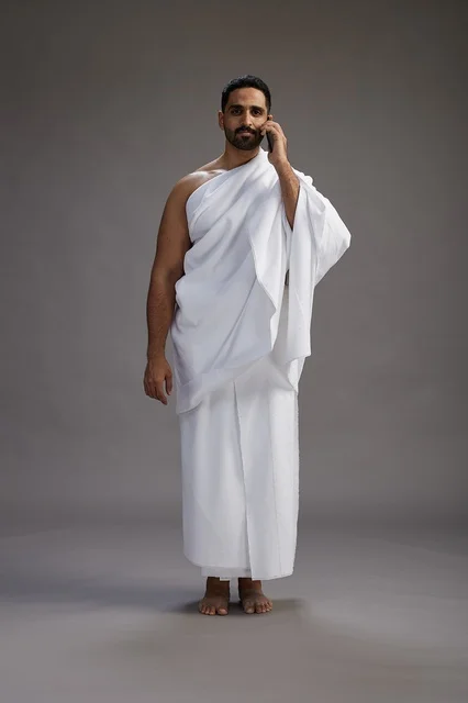 بورتريه لرجل سعودي بملابس الإحرام يجري مكالمة هاتفية عبر الهاتف المحمول, الاستعداد لاداء مناسك الحج والعمره, الجسم بالطول الكامل , خلفيه رماديه