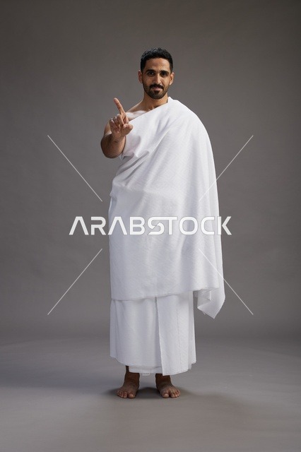 بورتريه لرجل عربي سعودي خليجي يرتدي ملابس الإحرام لأداء مناسك الحج, العباده والتقرب الى الله , الحج والعمره في مكه, الجسم بالطول الكامل , خلفيه رماديه