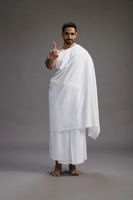 بورتريه لرجل عربي سعودي خليجي يرتدي ملابس الإحرام لأداء مناسك الحج, العباده والتقرب الى الله , الحج والعمره في مكه, الجسم بالطول الكامل , خلفيه رماديه