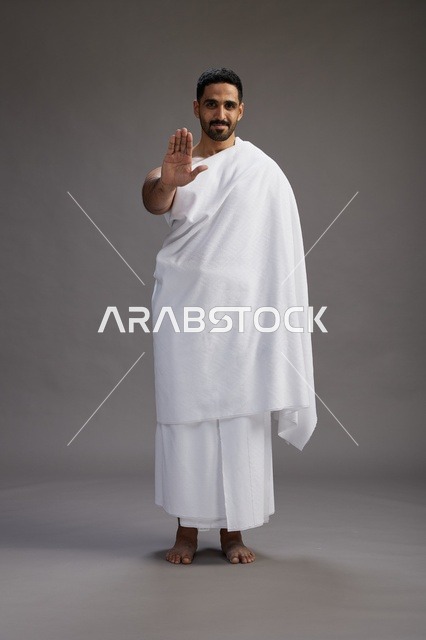 بورتريه لرجل عربي سعودي خليجي يرتدي ملابس الإحرام لأداء مناسك الحج, العباده والتقرب الى الله , الحج والعمره في مكه, الجسم بالطول الكامل , خلفيه رماديه