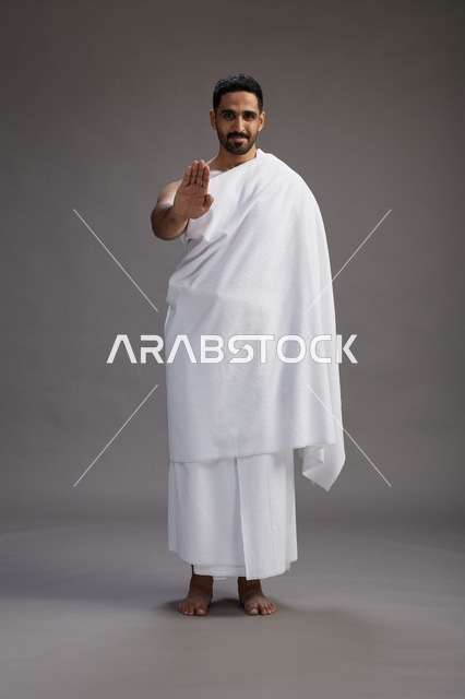 بورتريه لرجل عربي سعودي خليجي يرتدي ملابس الإحرام لأداء مناسك الحج, العباده والتقرب الى الله , الحج والعمره في مكه, الجسم بالطول الكامل , خلفيه رماديه