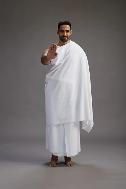بورتريه لرجل عربي سعودي خليجي يرتدي ملابس الإحرام لأداء مناسك الحج, العباده والتقرب الى الله , الحج والعمره في مكه, الجسم بالطول الكامل , خلفيه رماديه
