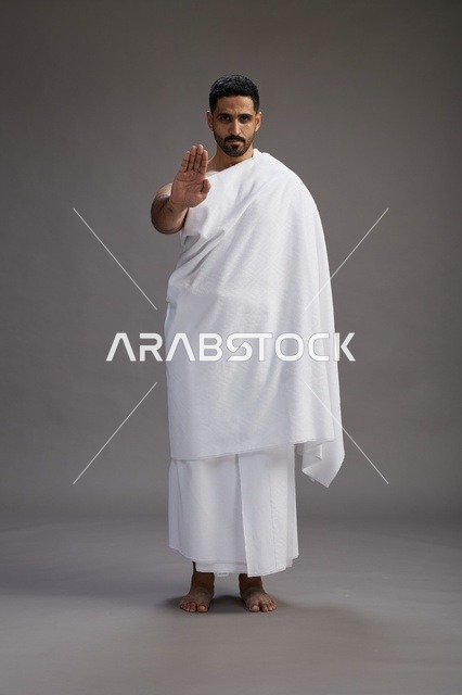 بورتريه لرجل عربي سعودي خليجي يرتدي ملابس الإحرام لأداء مناسك الحج, العباده والتقرب الى الله , الحج والعمره في مكه, الجسم بالطول الكامل , خلفيه رماديه