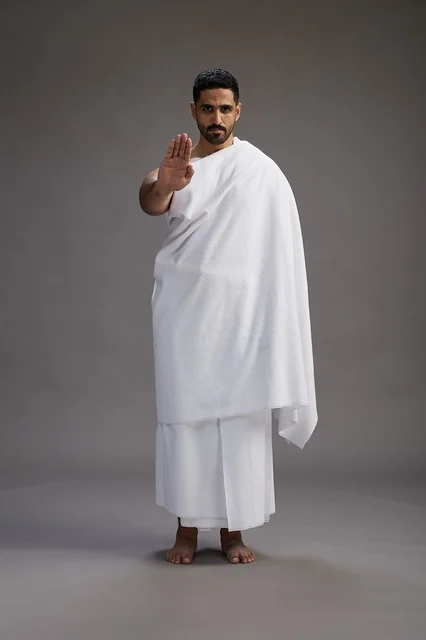 بورتريه لرجل عربي سعودي خليجي يرتدي ملابس الإحرام لأداء مناسك الحج, العباده والتقرب الى الله , الحج والعمره في مكه, الجسم بالطول الكامل , خلفيه رماديه