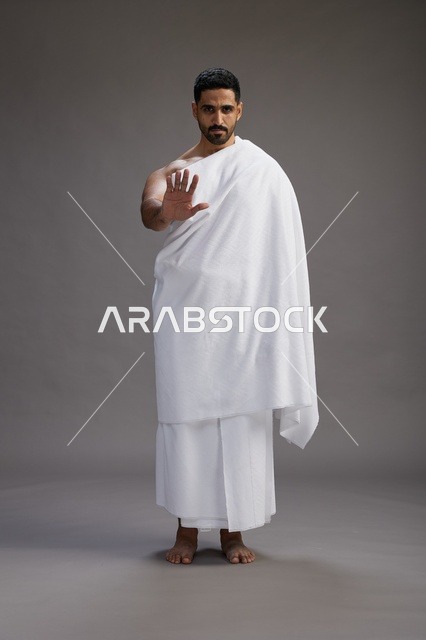 بورتريه لرجل عربي سعودي خليجي يرتدي ملابس الإحرام لأداء مناسك الحج, العباده والتقرب الى الله , الحج والعمره في مكه, الجسم بالطول الكامل , خلفيه رماديه