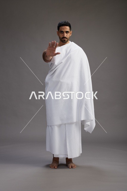 بورتريه لرجل عربي سعودي خليجي يرتدي ملابس الإحرام لأداء مناسك الحج, العباده والتقرب الى الله , الحج والعمره في مكه, الجسم بالطول الكامل , خلفيه رماديه