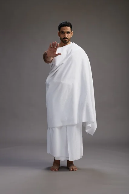 بورتريه لرجل عربي سعودي خليجي يرتدي ملابس الإحرام لأداء مناسك الحج, العباده والتقرب الى الله , الحج والعمره في مكه, الجسم بالطول الكامل , خلفيه رماديه