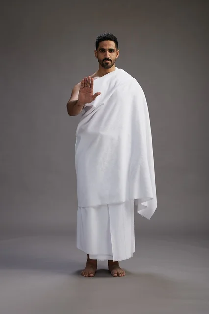 A portrait of an Arab Saudi Gulf man wearing Ihram clothing to perform the rituals of Hajj, worship, and drawing closer to God, Hajj and Umrah in Mecca, full-body, gray background.