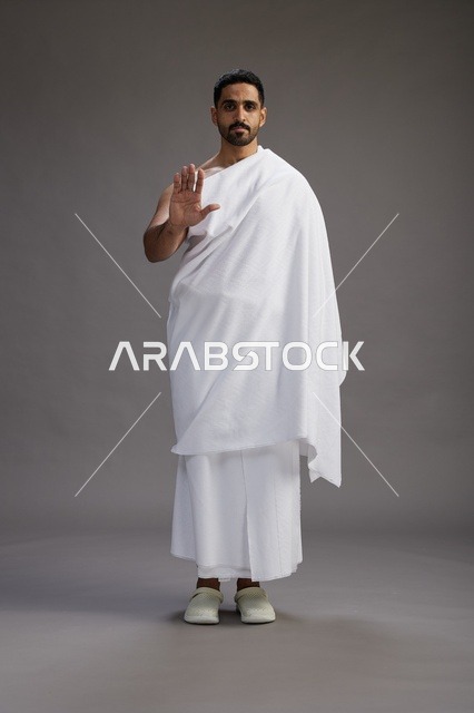 بورتريه لرجل عربي سعودي خليجي يرتدي ملابس الإحرام لأداء مناسك الحج, العباده والتقرب الى الله , الحج والعمره في مكه, الجسم بالطول الكامل , خلفيه رماديه