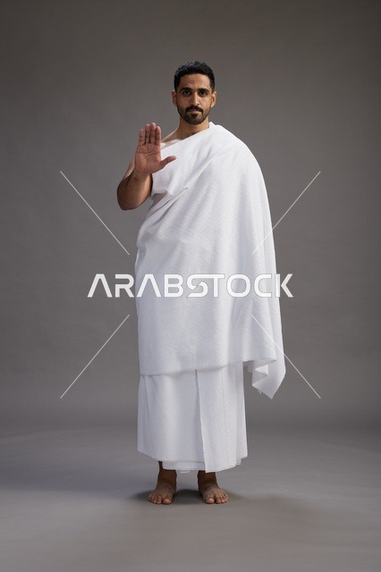 بورتريه لرجل عربي سعودي خليجي يرتدي ملابس الإحرام لأداء مناسك الحج, العباده والتقرب الى الله , الحج والعمره في مكه, الجسم بالطول الكامل , خلفيه رماديه